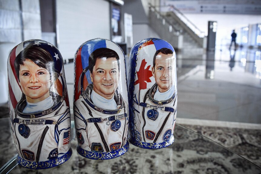 Three wooden dolls with portraits of astronauts on them sit on a table in a large room.