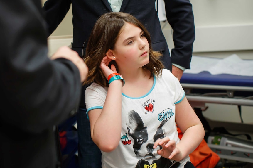 Young girl walks out of hospital wearing ID wrist bands and a T-shirt featuring a dog.