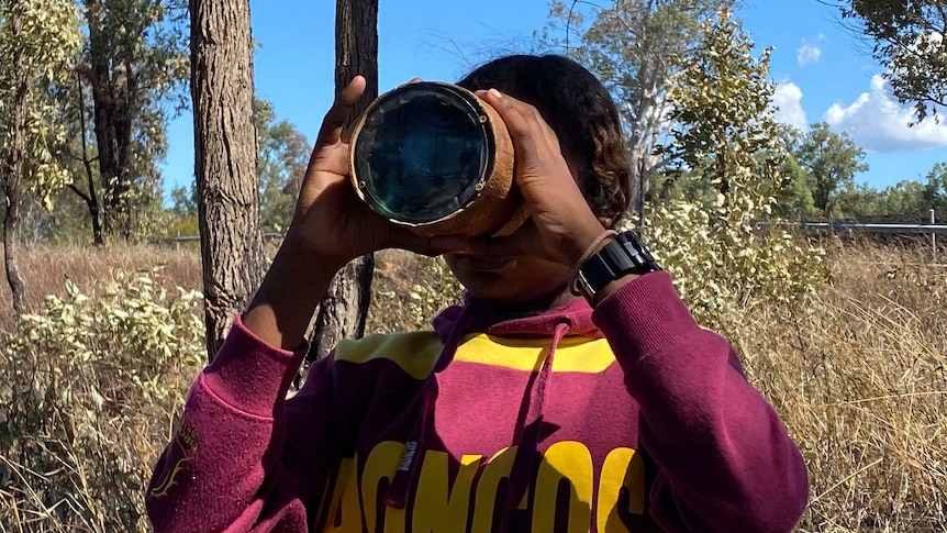 a student looks through a magnifying glass at the end of a hollowed log