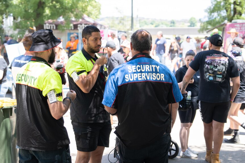 Three men wearing shirts that say "security". 