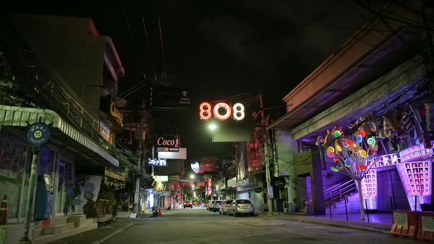 An empty street with shops and signs lit up with neon lights.