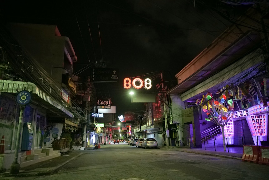 An empty street with shops and signs lit up with neon lights.