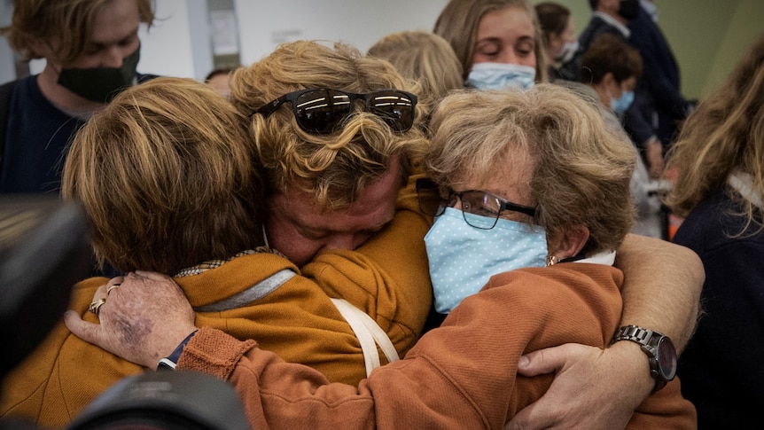 Three people embracing at an airport.
