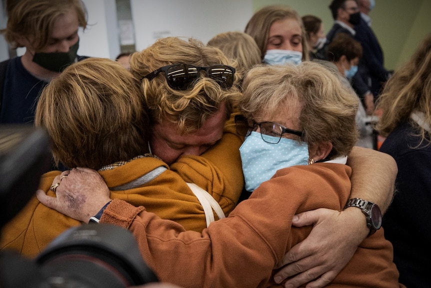 Three people embracing at an airport.