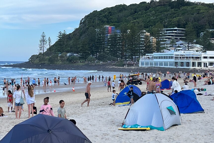 a crowd of people stand on the beach at Burleigh with people cleared out of the water