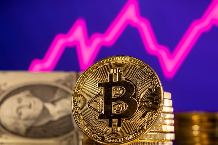 A representation of bitcoin is seen in front of a stock graph and US dollar 