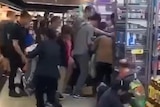 A scene showing people being knocked to the ground in a scramble to grab cans of baby formula from the shelves.