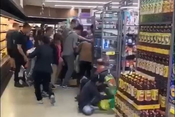 A scene showing people being knocked to the ground in a scramble to grab cans of baby formula from the shelves.
