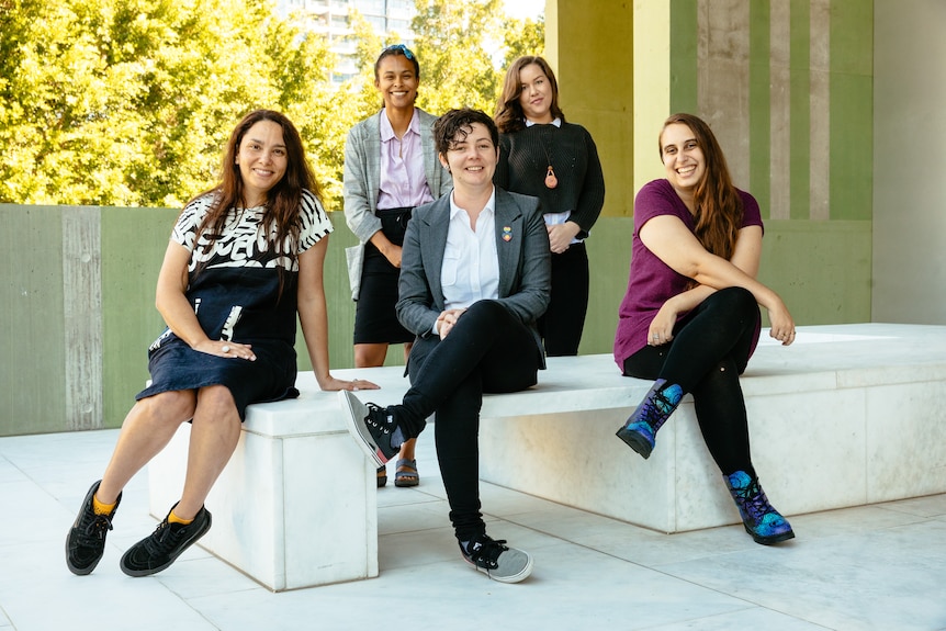 A group of five young Aboriginal women all sitting outside a library