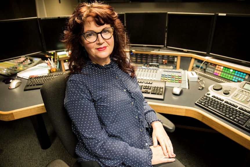 A woman sits at a screen editing booth