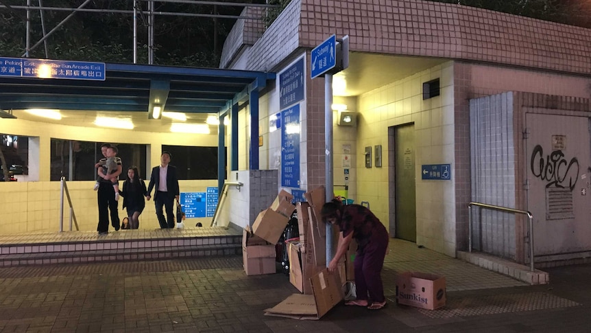 An old woman collecting flattened cardboard by a train station
