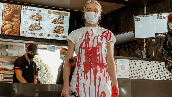 Tash Peterson in all white covered in fake blood inside a fast food restaurant.