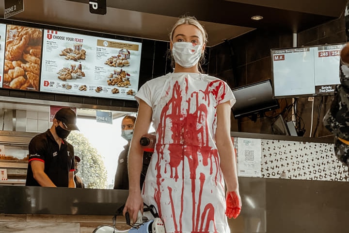 Tash Peterson in all white covered in fake blood inside a fast food restaurant.