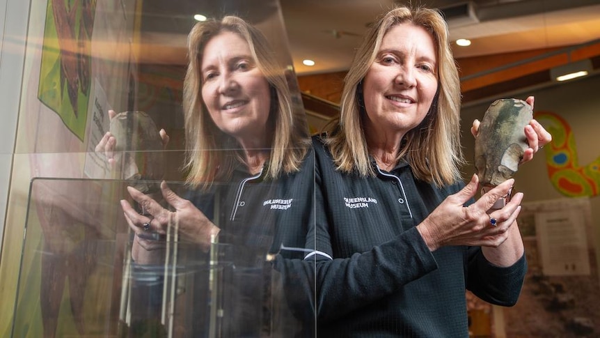 A woman wearing a shirt that says MUSEUM holds up an object next to a glass cabinet