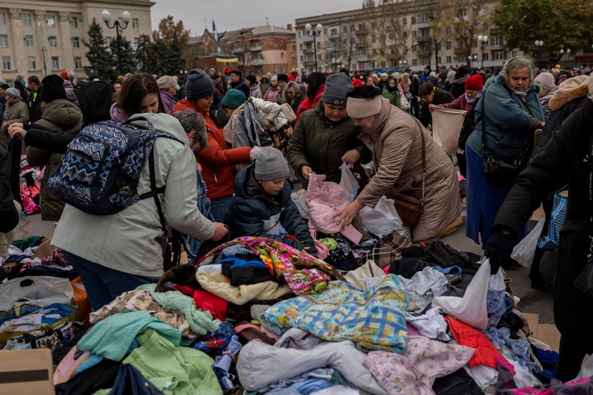 People crowd around piles of clothes. 