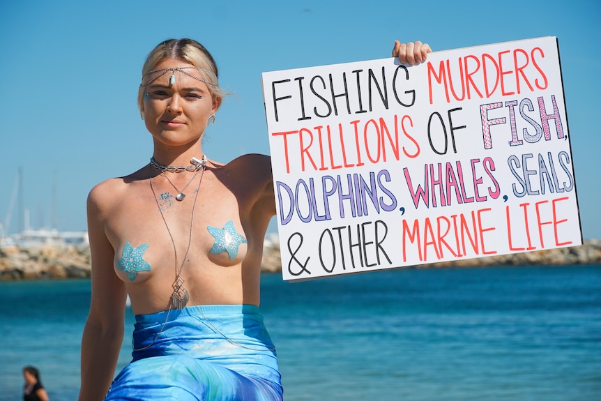 Tash Peterson wearing a mermaid skirt and topless except for her nipples holding a sign on the "murder" marine life