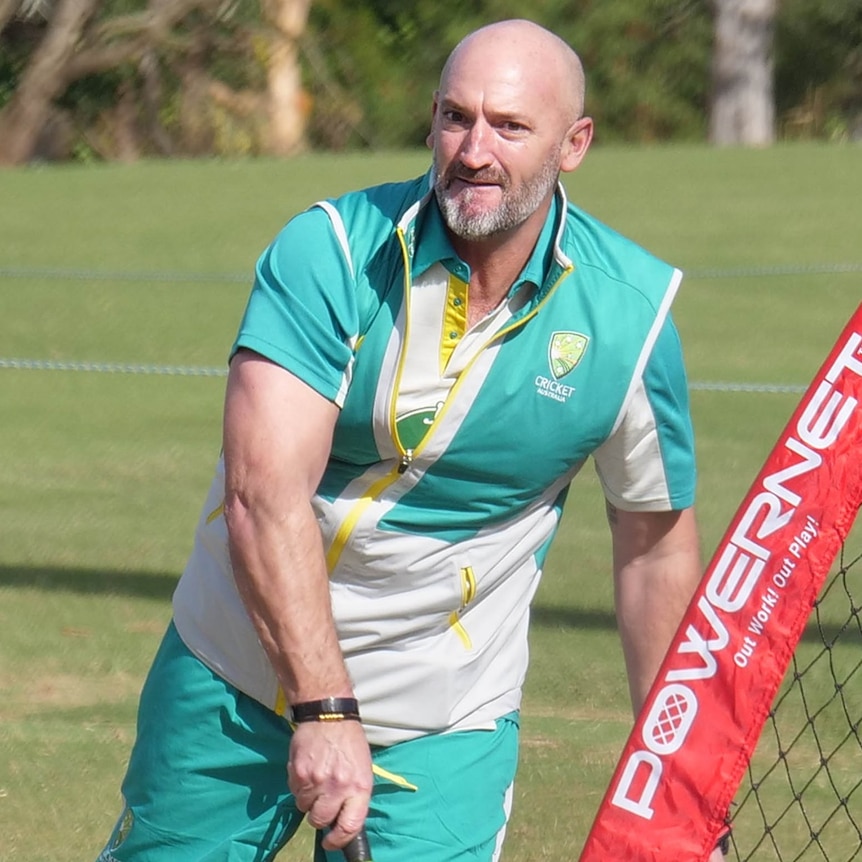 A bald man, wearing a green cricket Australia top throws a cricket ball at training. 