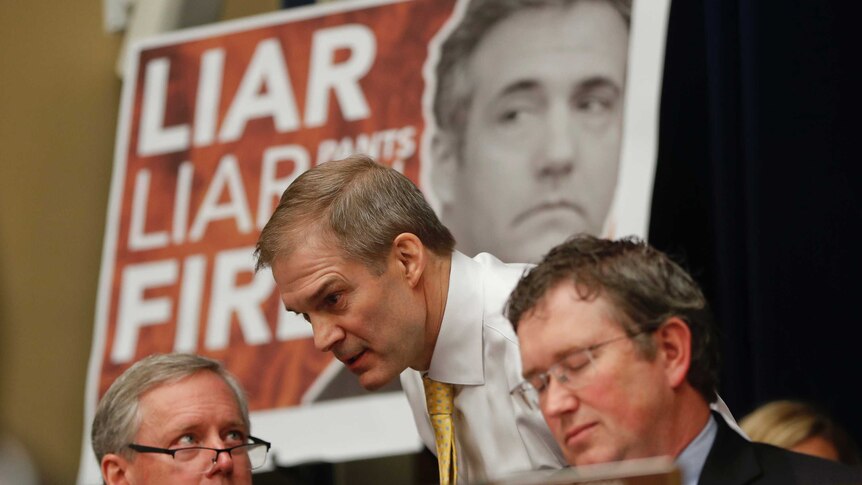 Jim Jordan speaks to other congressmen while a 'LIAR, LIAR, PANTS ON FIRE' sign with Michael Cohen's face on it sits behind him.