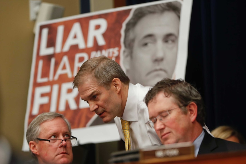 Jim Jordan speaks to other congressmen while a 'LIAR, LIAR, PANTS ON FIRE' sign with Michael Cohen's face on it sits behind him.