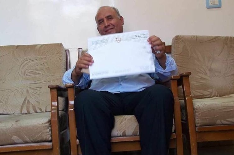 Ismail Khalif sits on a couch and poses for a photo holding a parcel.