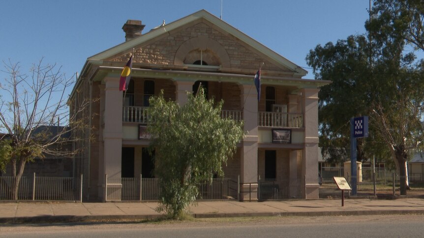 A sandstone building with an aboriginal and Australian flag handing from it. 