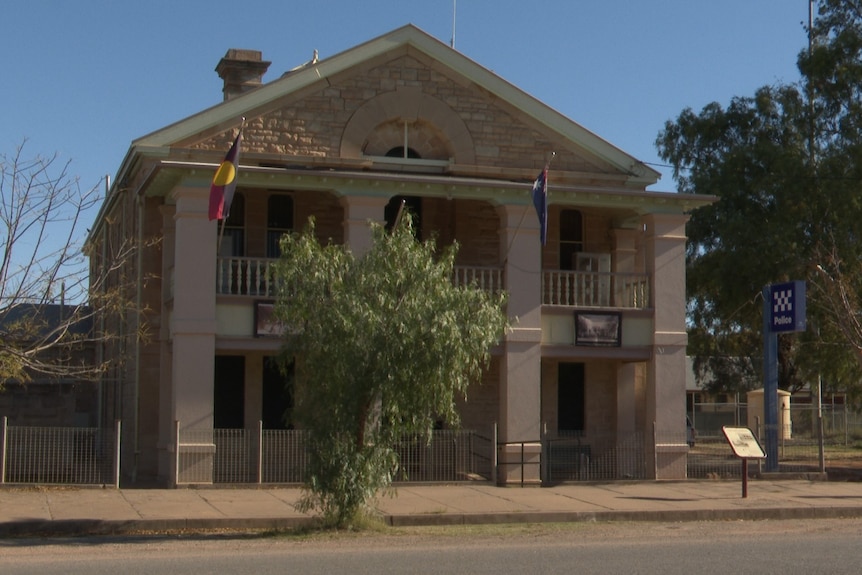 A sandstone building with an aboriginal and Australian flag handing from it. 