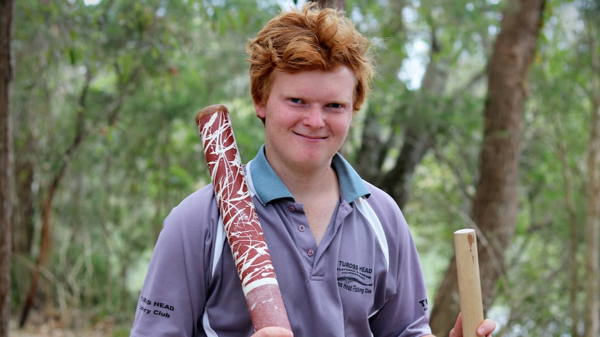 Red-haired and pale-skinned Indigenous teenager Michael James holding a didgeridoo and clap stick