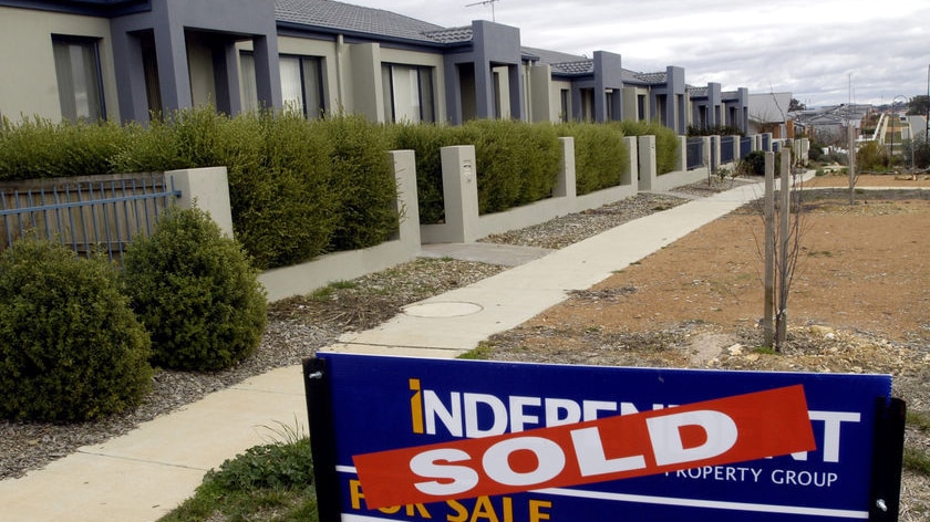 A row of houses in a Canberra suburb with a sold sign in front of one.