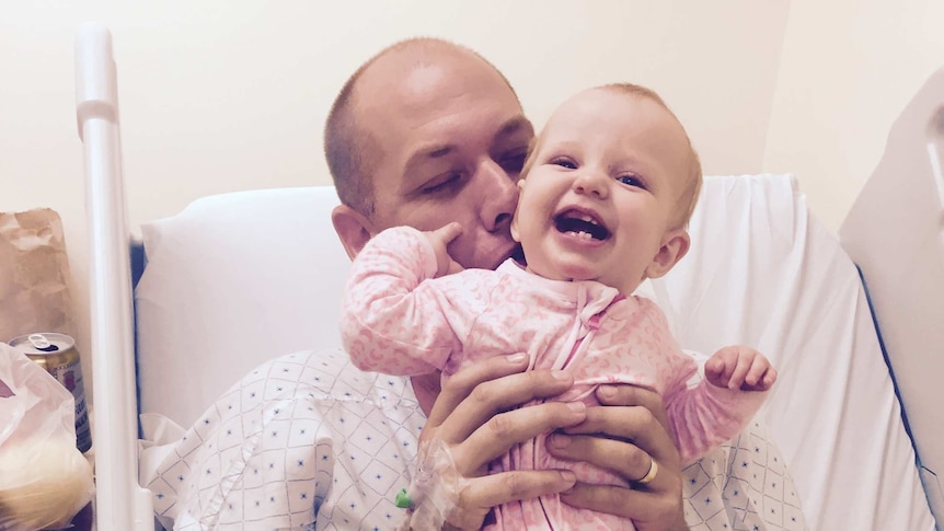 Adam Harvey with his daughter Isla in hospital after having a bullet removed from his neck