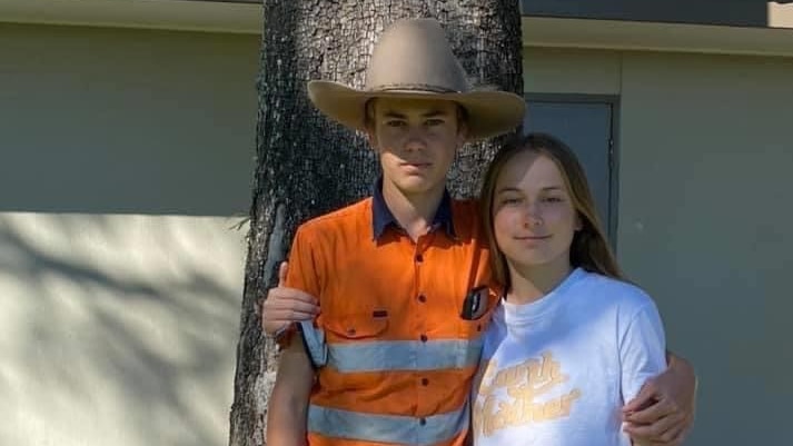 A teenage boy wearing a high-vis shirt and cowboy hat stands with his arm around his teenage sister.