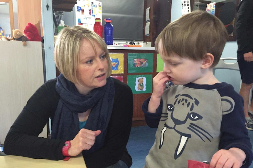A blonde woman in dark blue jumper and scarf sitting next to young boy in tiger jumper