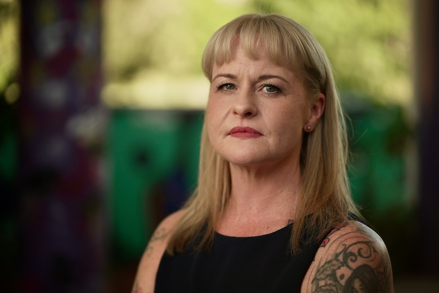 A woman with blonde hair with tattoos looks at the camera from the side.