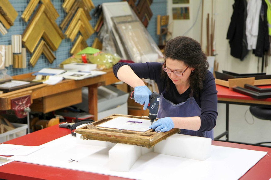 Holly uses a drill to remove the back of an artwork.