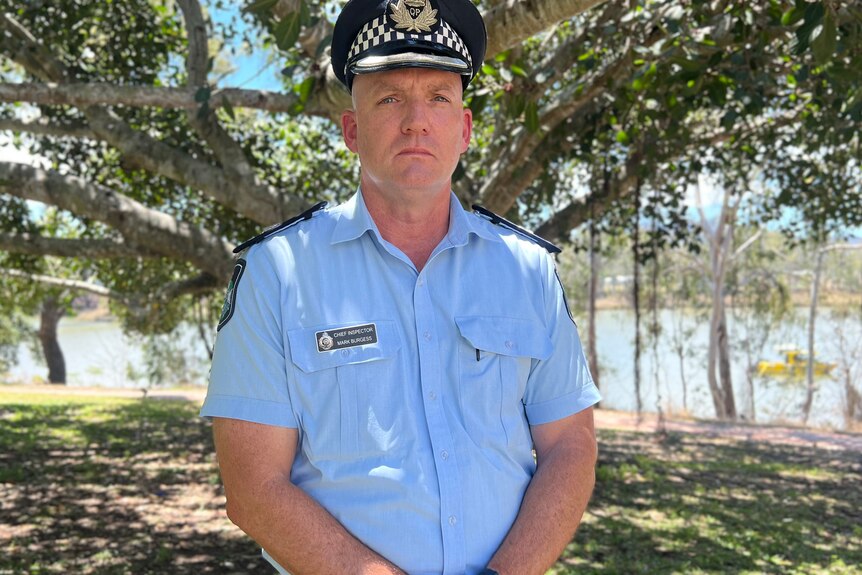A uniformed police officer standing in front of a tree looking at the camera