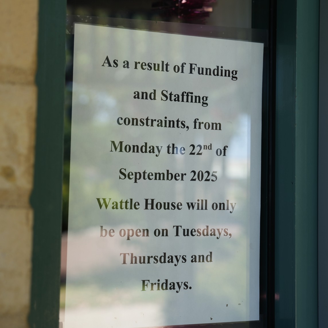 A sign on a wall telling people that due to funding cuts a charity will only be opening three days a week.