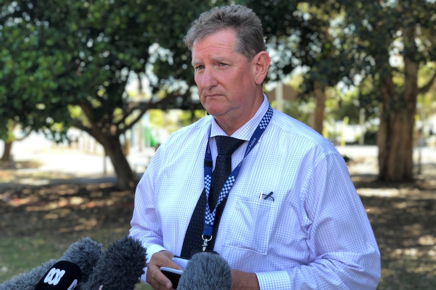 A middle-aged man with greying hair and business shirt & tie, looks to distance with mics in front.