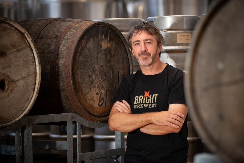 A man stands with his arms crossed in a room full of barrels.