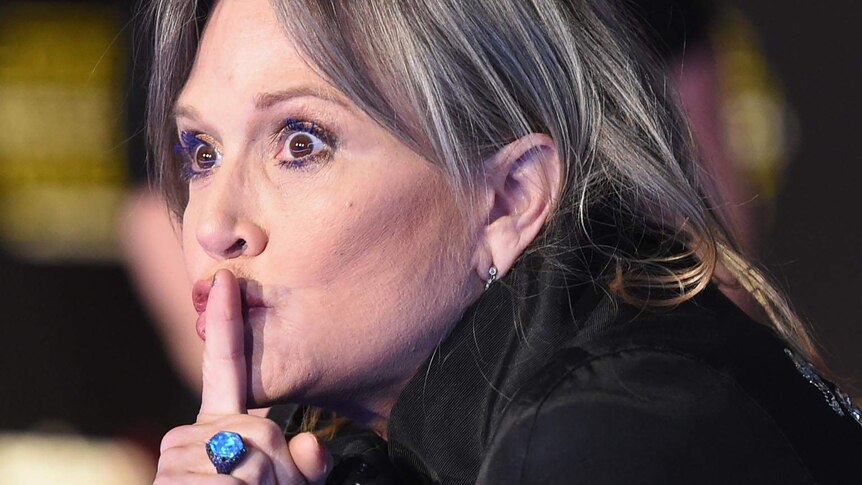 Carrie Fisher makes a shhh gesture on the red carpet at the premiere of Star Wars: The Force Awakens.