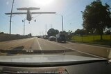 View from the inside of a car on a street, with a small plane less than the height of power poles away.