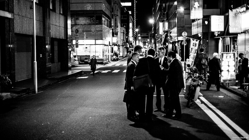 Men in suits stand in a circle talking on the road