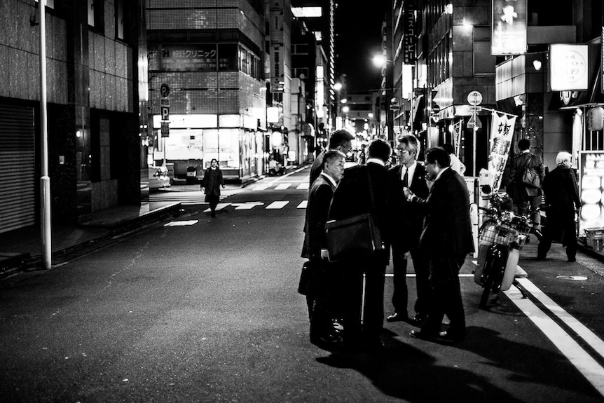 Men in suits stand in a circle talking on the road