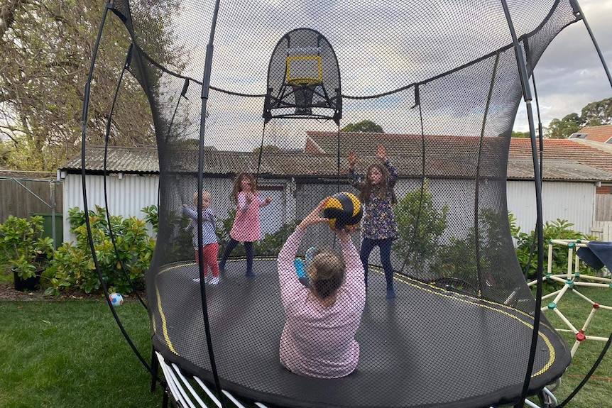 Elissa Ken plays on the trampoline throwing a ball to her three kids.