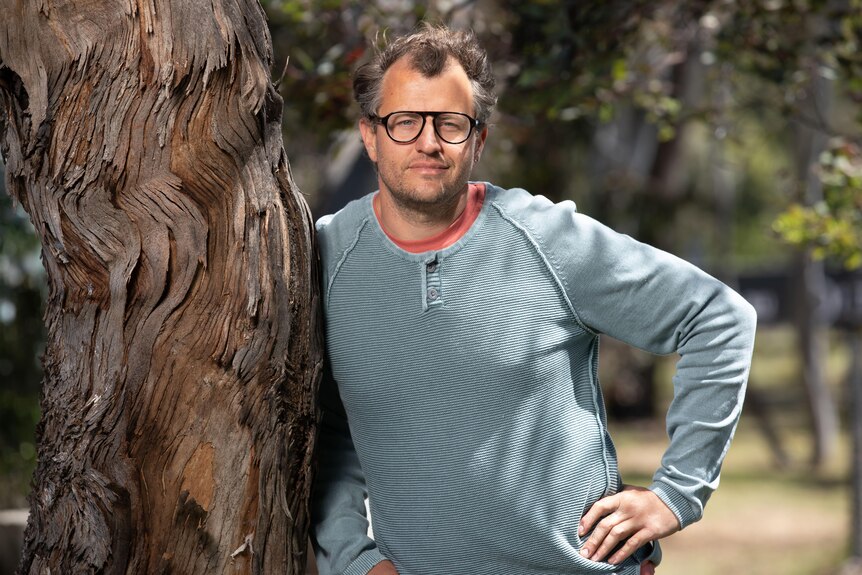A man wearing glasses and a grey jumper smiles for the camera
