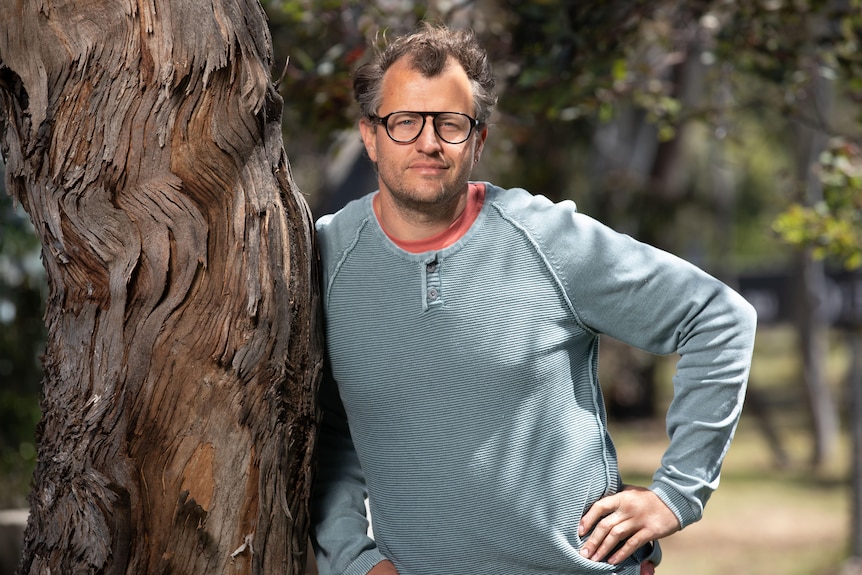 A man wearing glasses and a grey jumper smiles for the camera