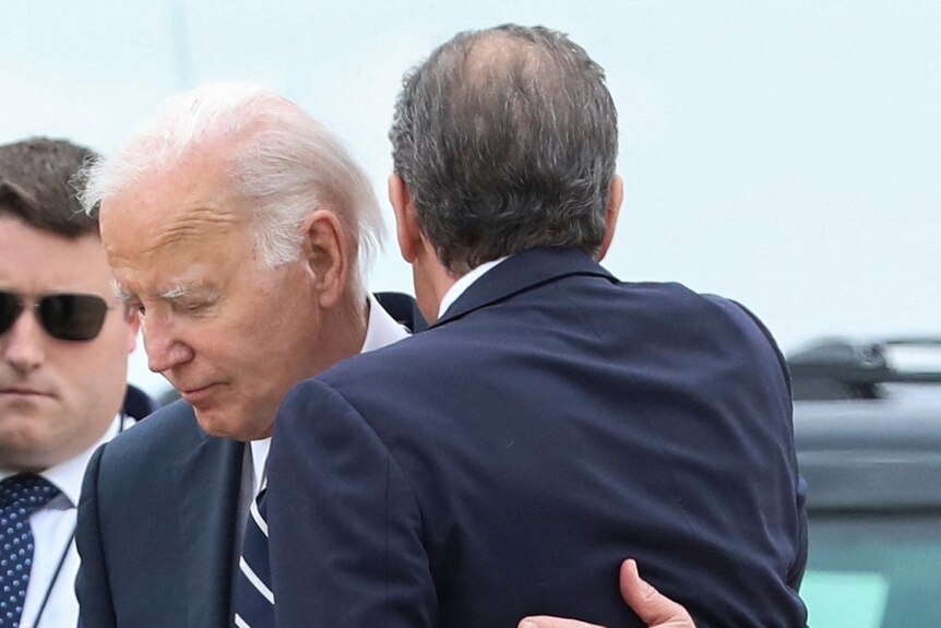 Joe Biden hugs Hunter Biden. A black car is in the background.