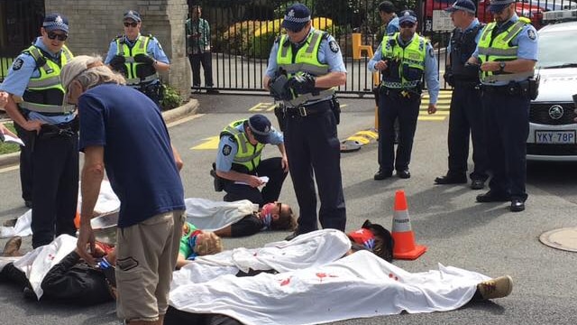 Protestors lie on the road covered in white sheets stained with red dye, at the Indonesian Embassy in Canberra.