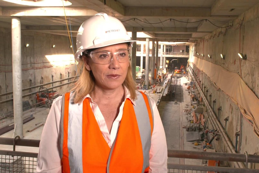 Rita Saffioti wearing a white shirt, high vis orange safety vest and white hard hat, standing in partially completed rail tunnel