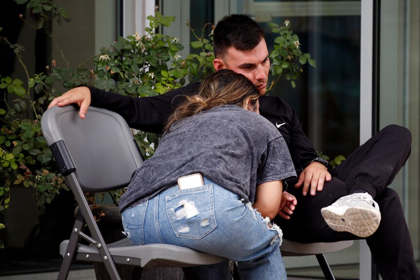 A woman leans on a man as they sit on plastic chairs