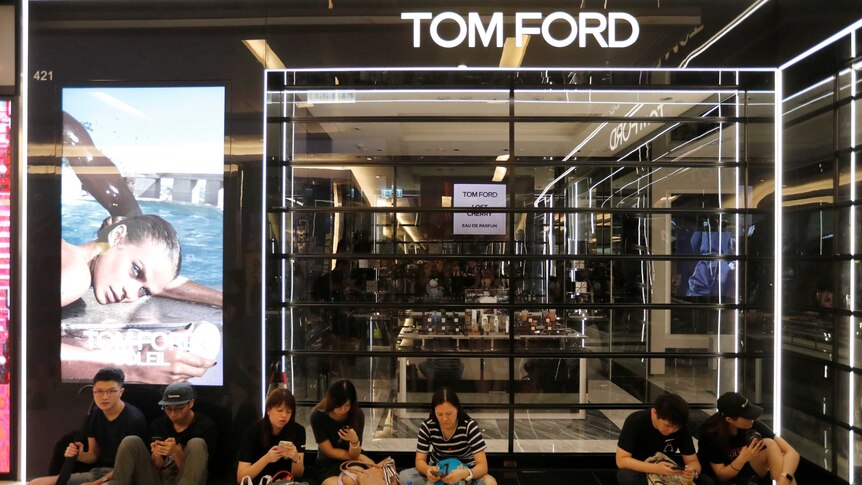 A group of people sit on the floor outside a closed Tom Ford boutique