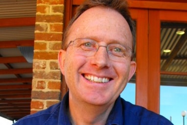 A man wearing glasses smiles at the camera.